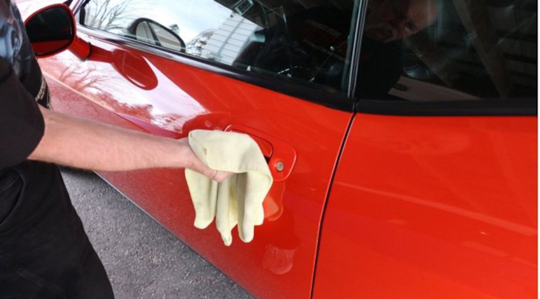 A person cleaning a car door handle with a cloth